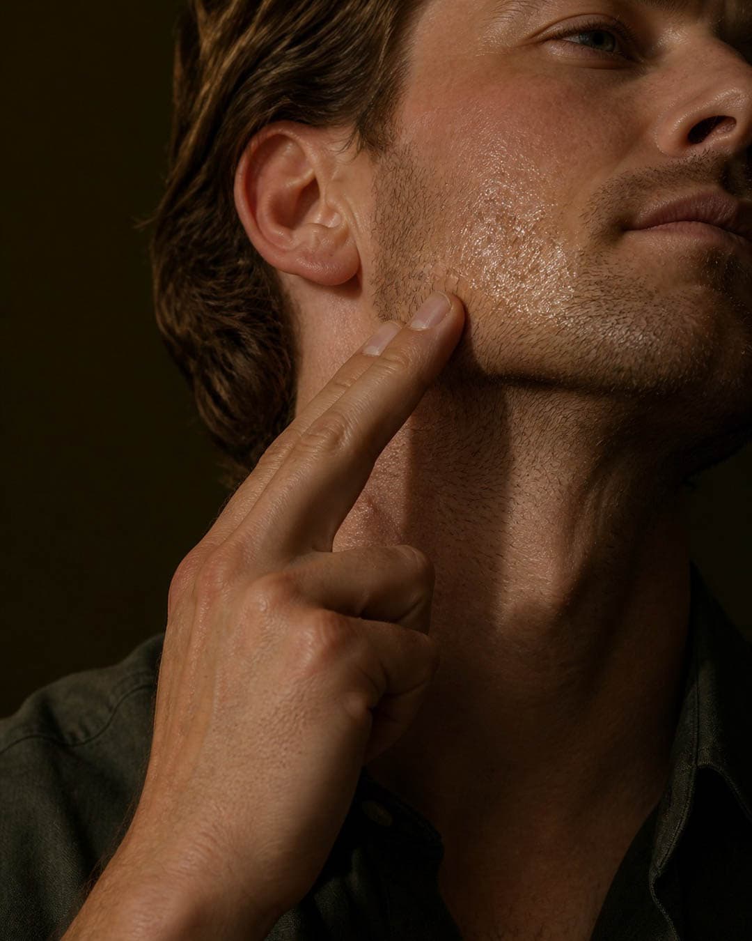 A man pressing oil up along his jaw in low evening light
