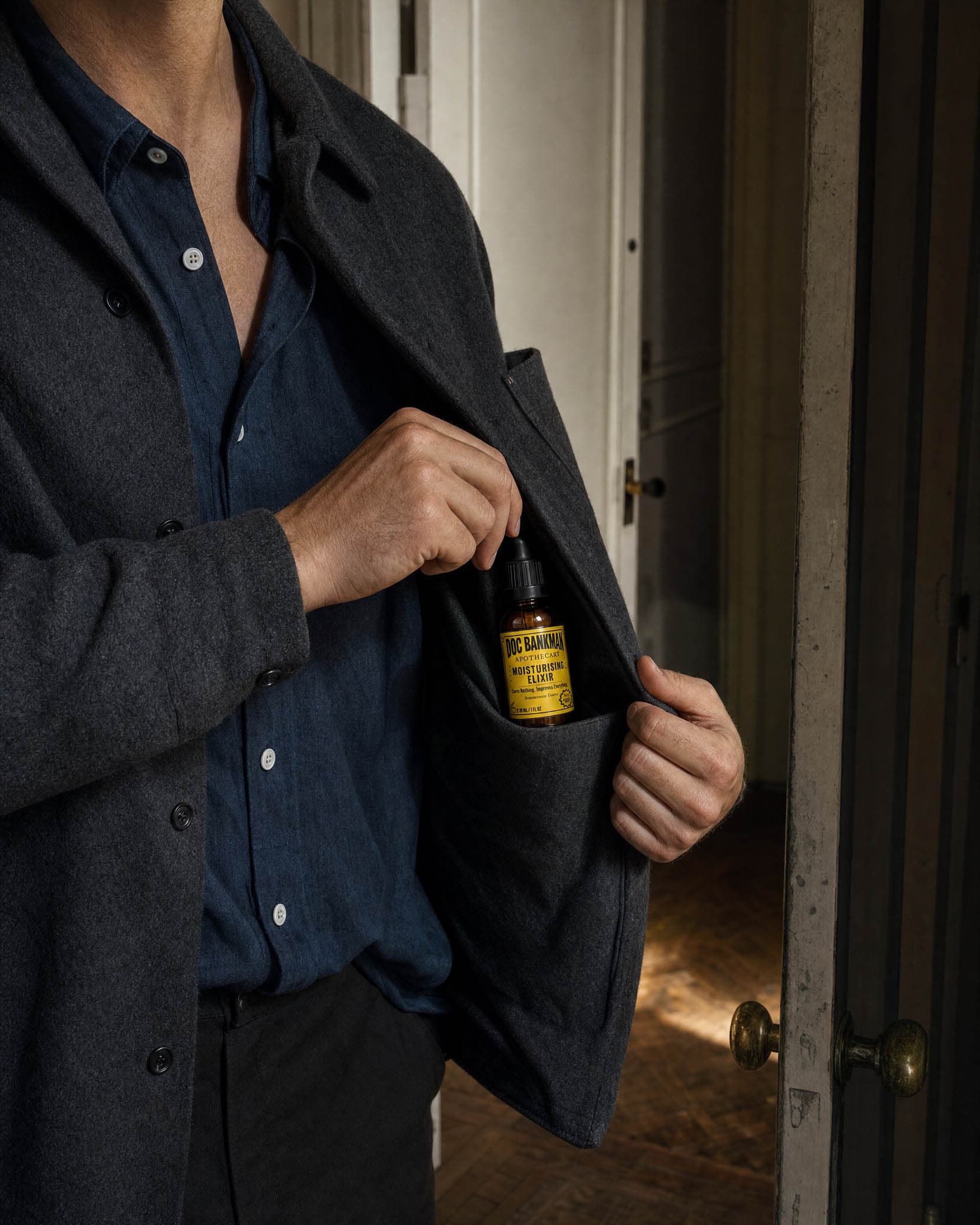 A man slipping the bottle into the inside pocket of a wool jacket by the front door