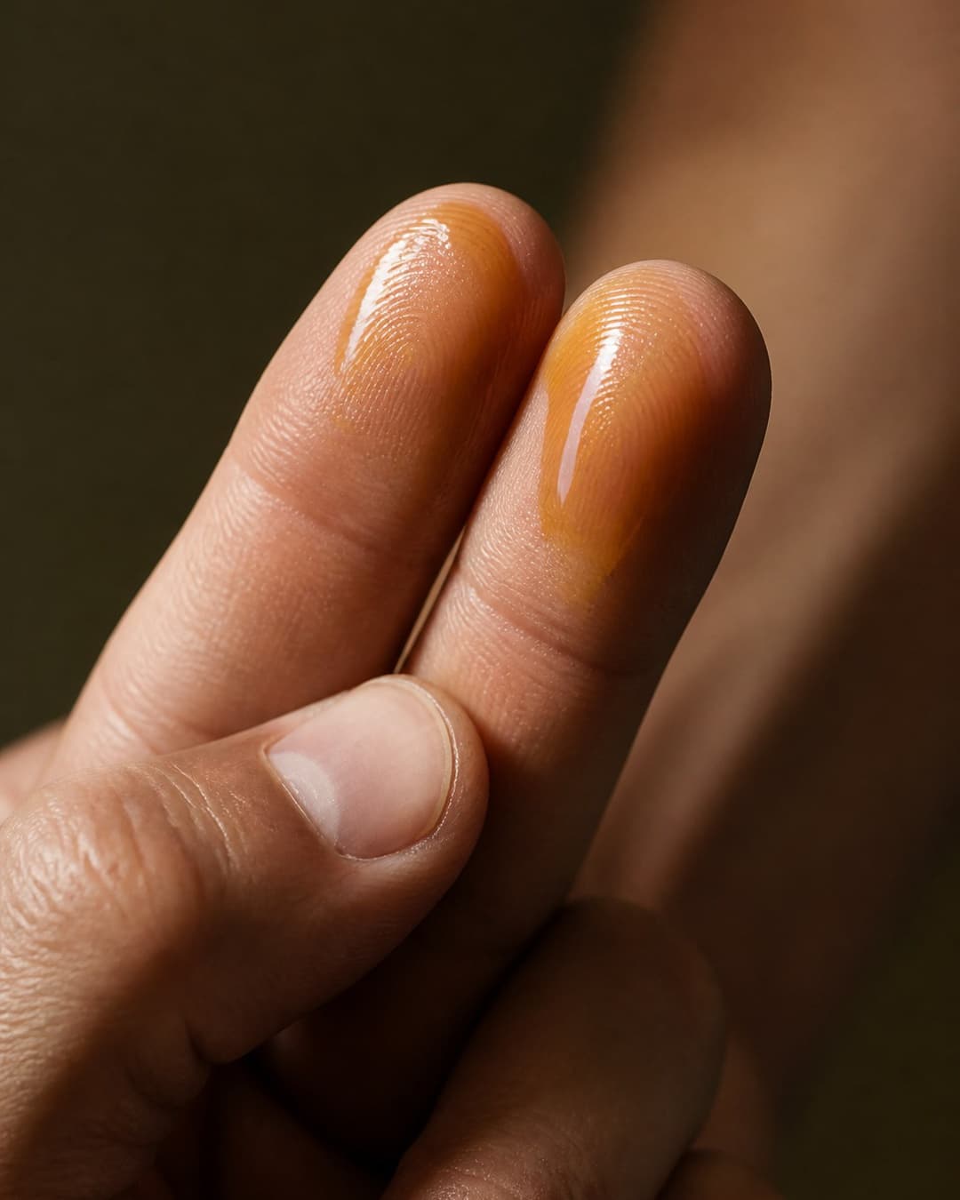 Oil across the pads of two fingertips, close up